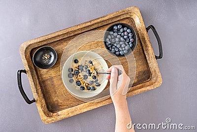 Womanâ€™s hand stirring a healthy breakfast of cooked oatmeal with fresh walnuts and blueberries Stock Photo